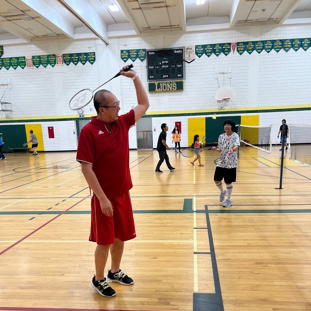 Badminton players rallying in a school gym during a Scuola sports session.