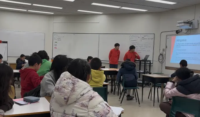 Students watching presenters and a slide deck during a Scuola debate workshop.